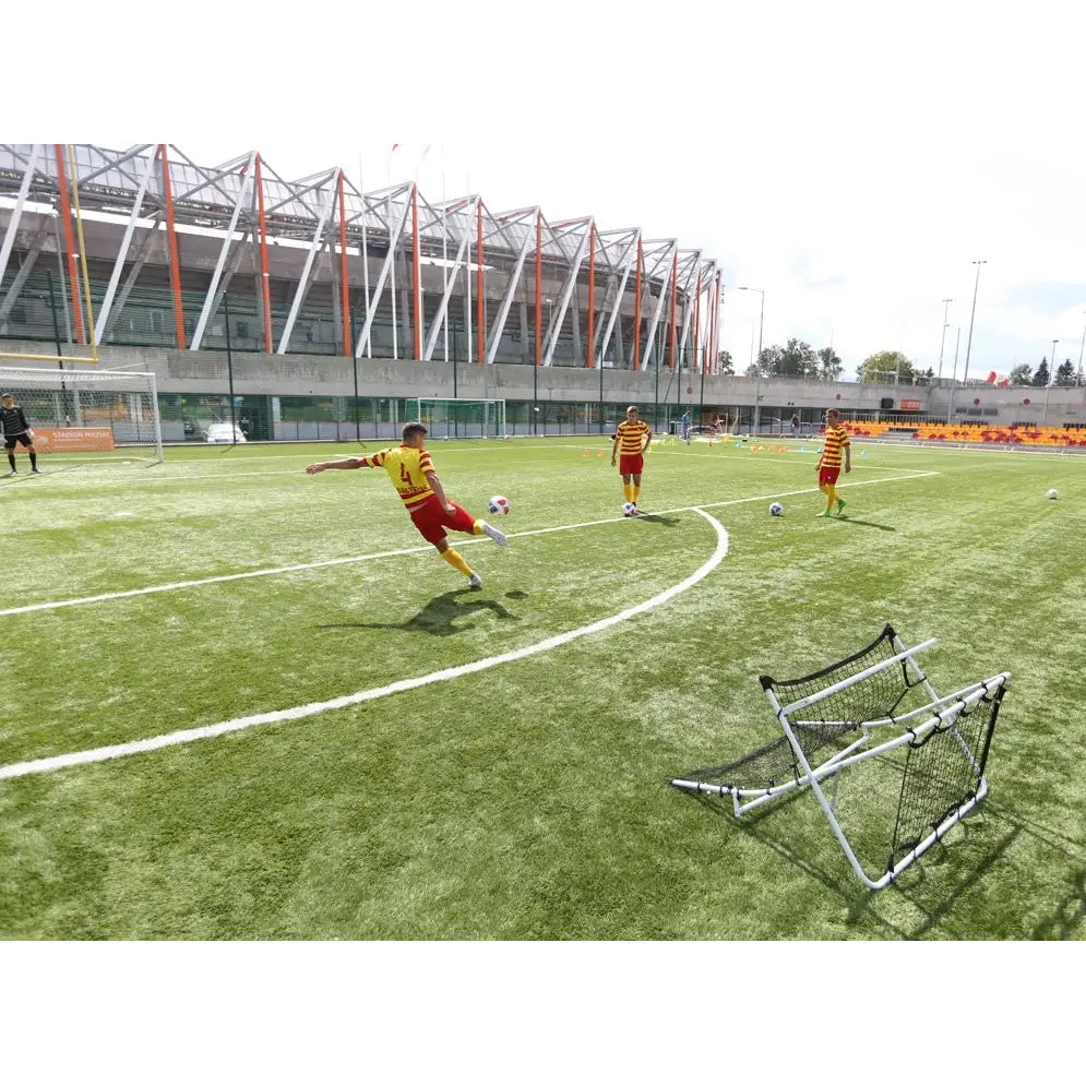 Fotball rebounder med sort nett og aluminiumsramme, brukt på kunstgressbane under fotballtrening.