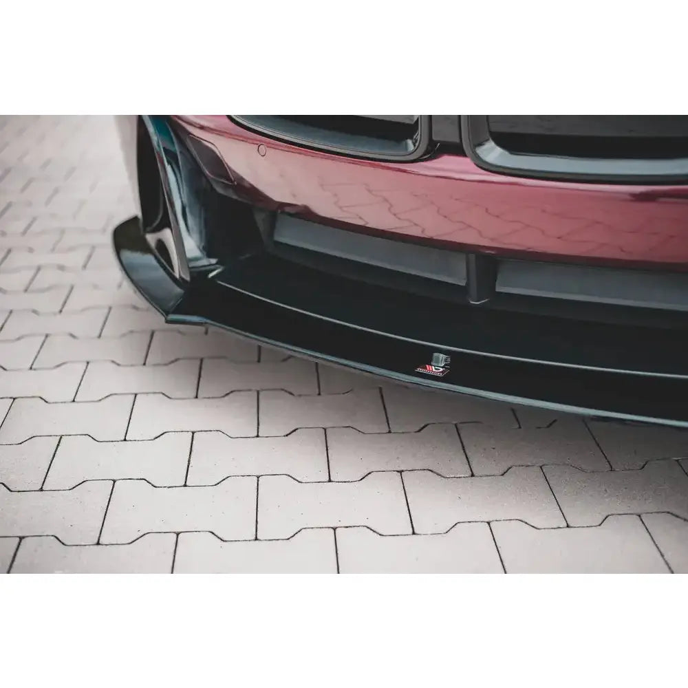 Front splitter på sort, blank BMW I8-frontspoiler med logo, montert på burgunderrød bil, sett forfra.