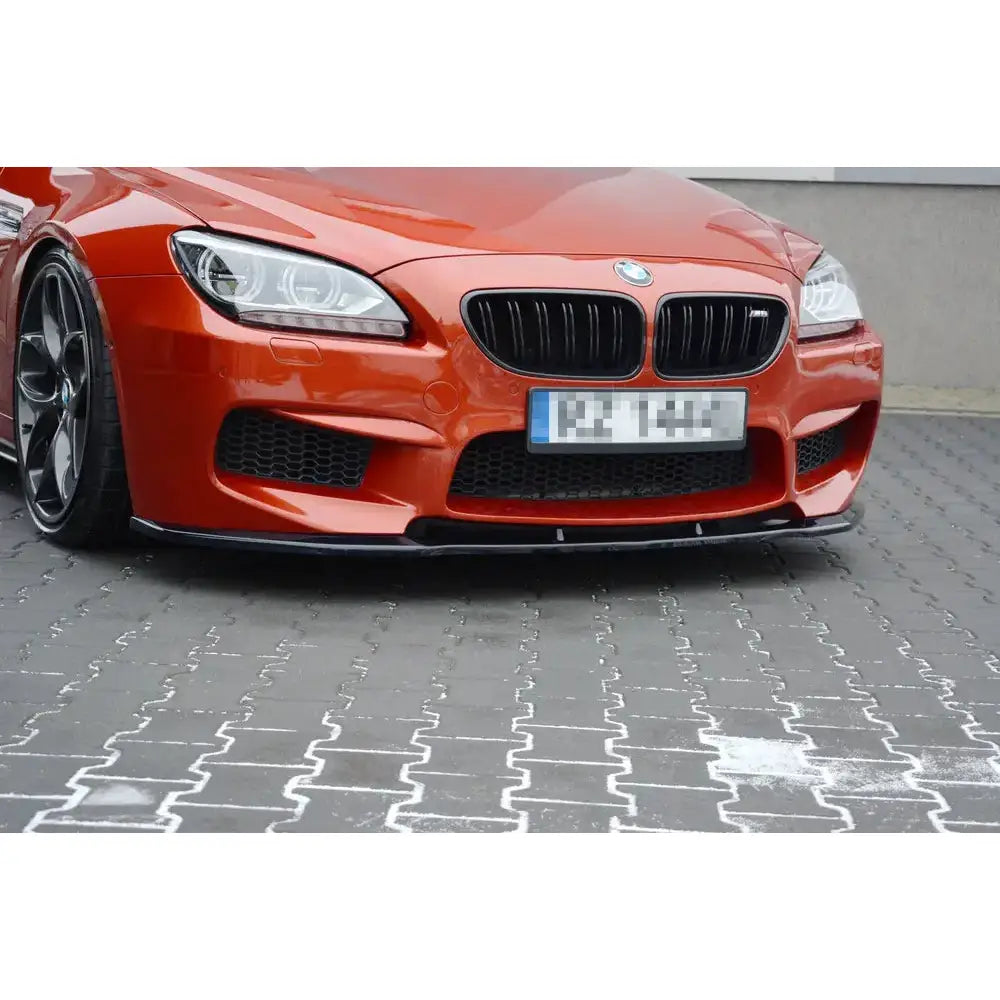Spoiler til BMW M6 Gran Coupé i blank svart finish montert foran på oransje bil, sett fra lav vinkel.