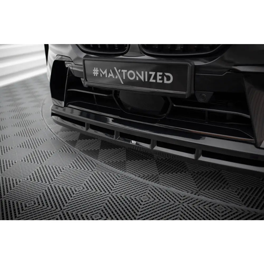 Spoiler til BMW X7 M-Pack G07 Facelift, sort og glanset, montert på bil over rutemønstret gulv.