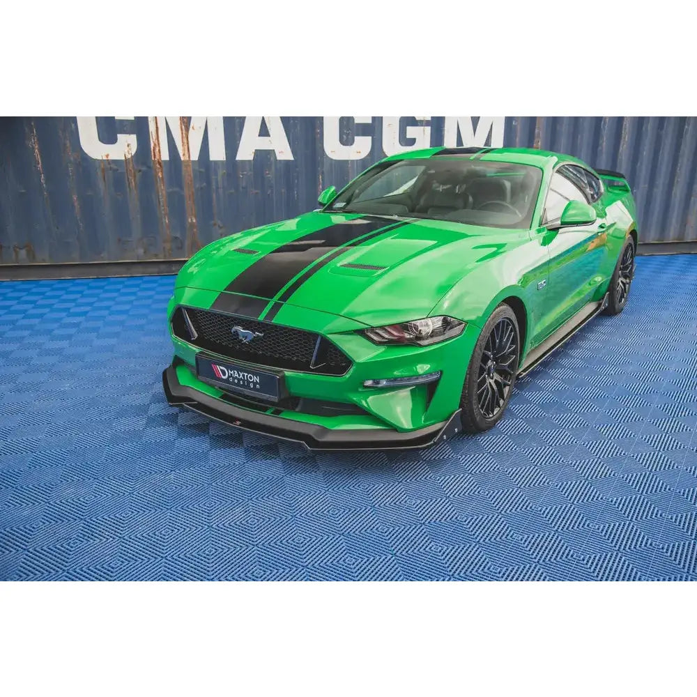 Front splitter på grønn Ford Mustang GT MK6 Facelift med svarte striper og felger, parkert på blått gulv.