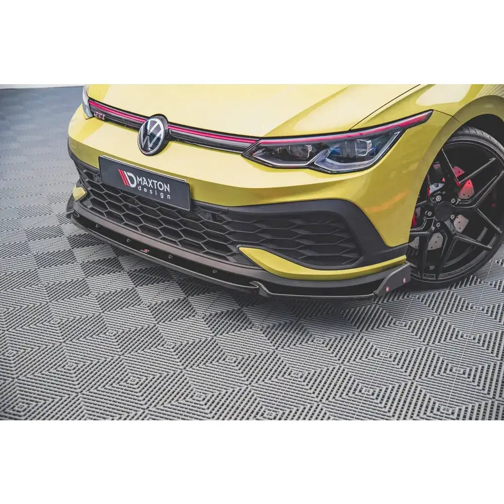 Front splitter på Volkswagen Golf 8 GTI Clubsport med karbon-look, sort grill og gul lakk på mønstret gulv.