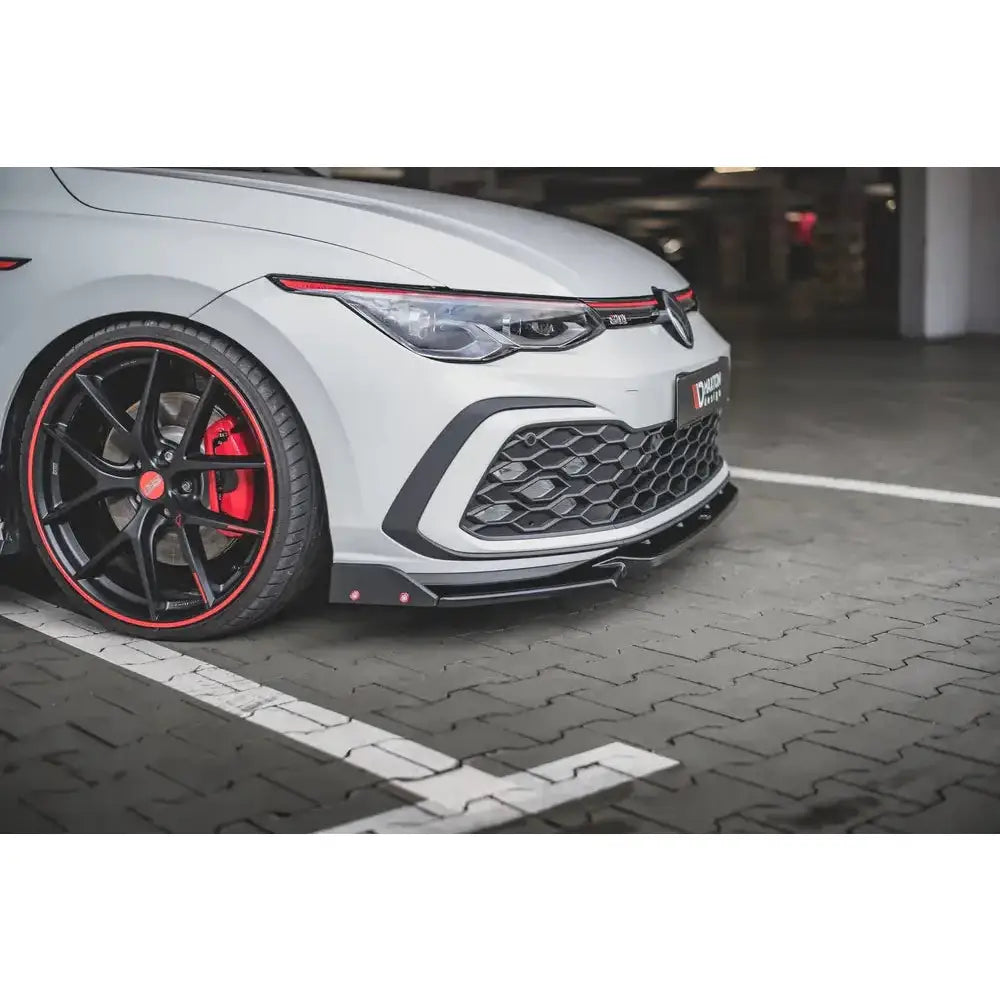 Spoiler Volkswagen Golf 8 GTI med svart frontskjørt, rød bremseskive og felg med rød kant.