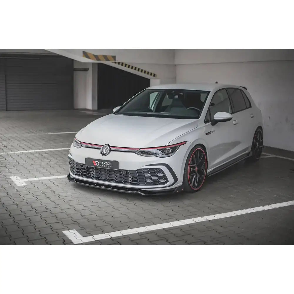 Front lip på Volkswagen Golf 8 GTI med sorte og røde detaljer, parkert innendørs.