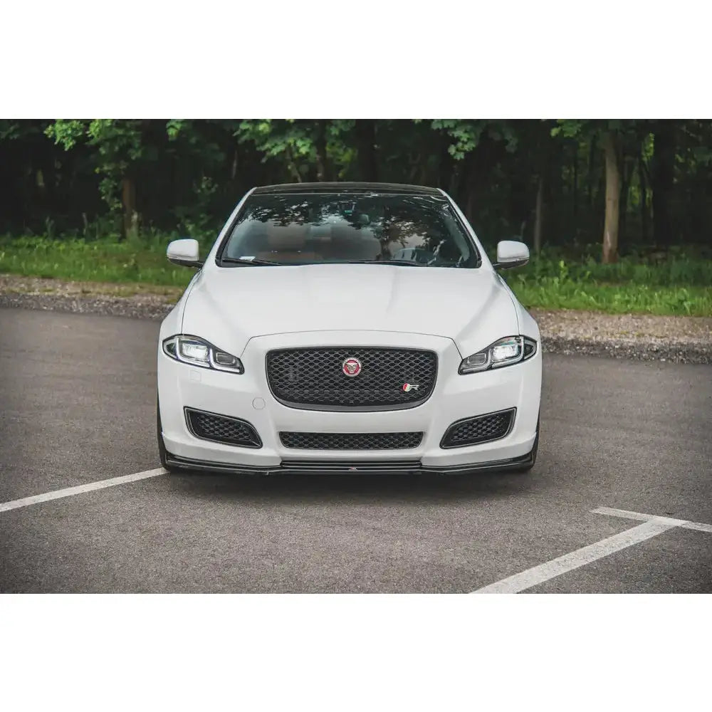 Frontleppe Jaguar XJ X351 Facelift sett forfra med sort grill og logo, parkert foran grønt buskas.
