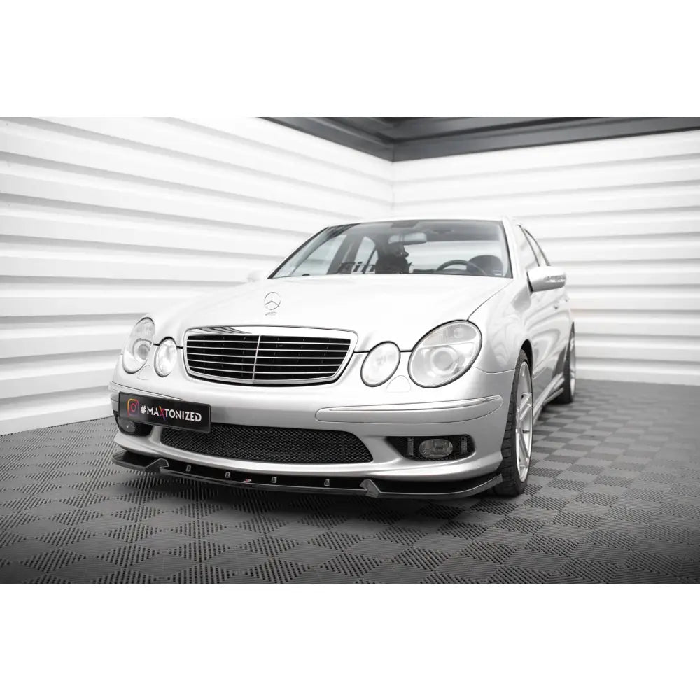 Frontleppe på Mercedes E 55 AMG W211, sølvfarget bil sett forfra fra venstre på svartmønstret gulv.