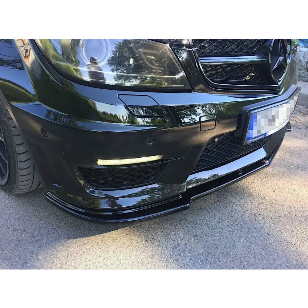 Frontspoiler Mercedes C63 AMG W204 Facelift i sort blank plast montert på bil, sett fra lav vinkel.