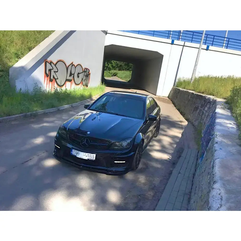 Front splitter på Mercedes C63 AMG W204 Facelift parkert foran graffitivegg og grønt gress.