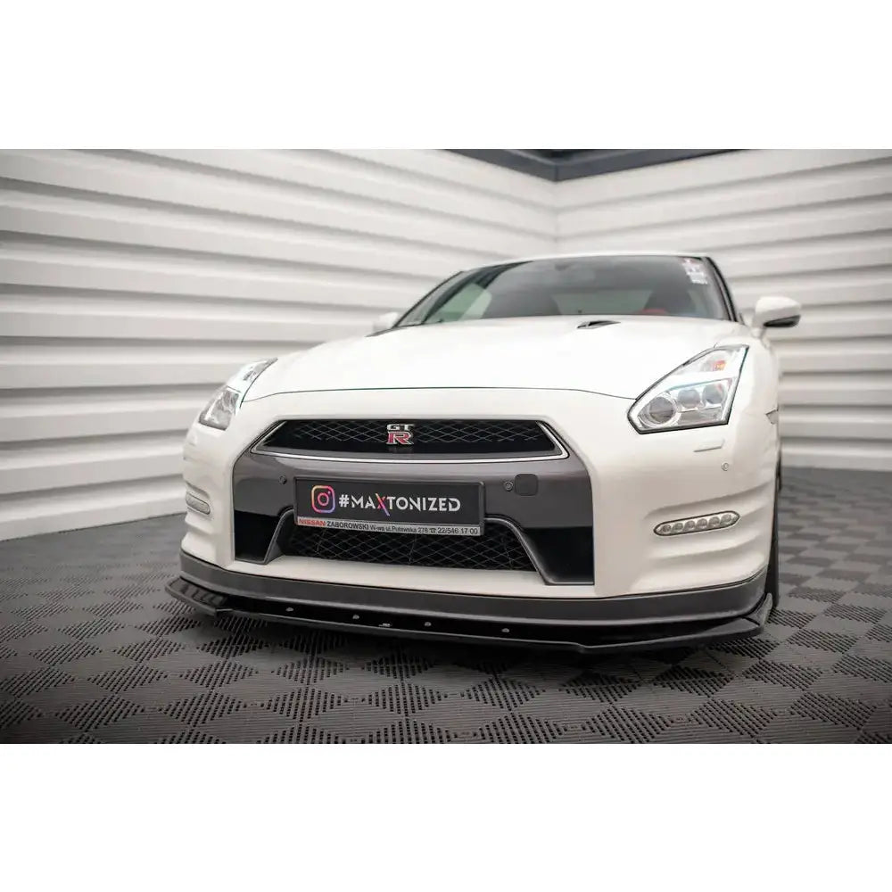 Front splitter på hvit Nissan GTR R35 Facelift 11-16 med sorte detaljer og GT-R-emblem, sett forfra.