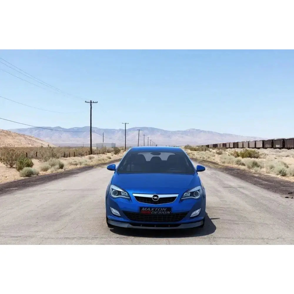 Frontleppe på Opel Astra J pre-facelift, blå bil parkert foran fjell og ørken, svart detalj under fangeren.