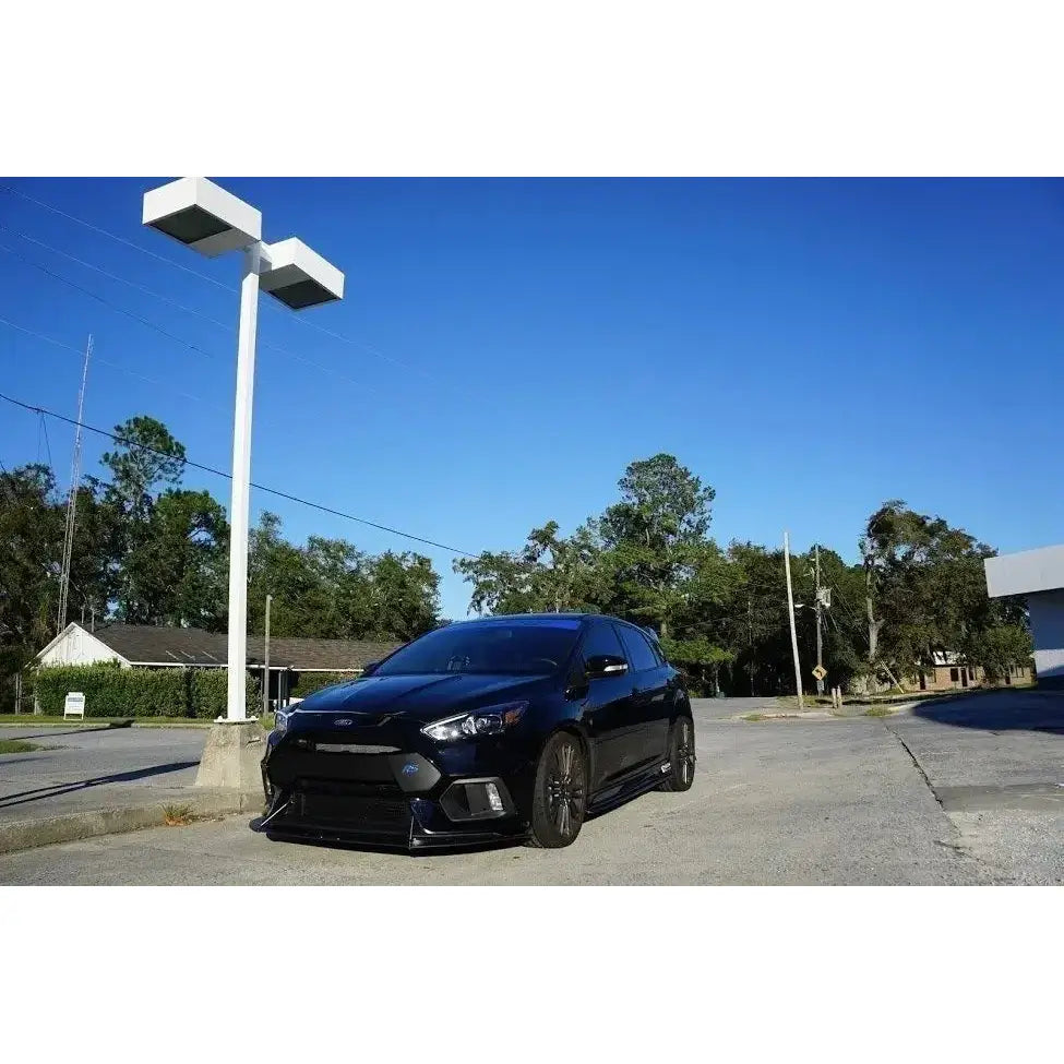 Frontleppe på svart Ford Focus 3 Rs med store felger, sett skrått forfra under blå himmel.