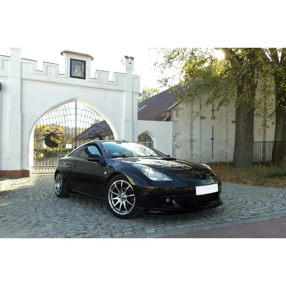 Frontspoiler Toyota Celica T23 Preface V.2 Racing svart bil på brostein med sølvfelger og hvit murport.