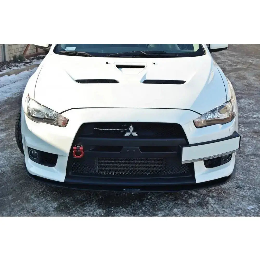 Front splitter på Mitsubishi Lancer Evo X Racing med sort grill, rød tauekrok og snødekt asfalt.