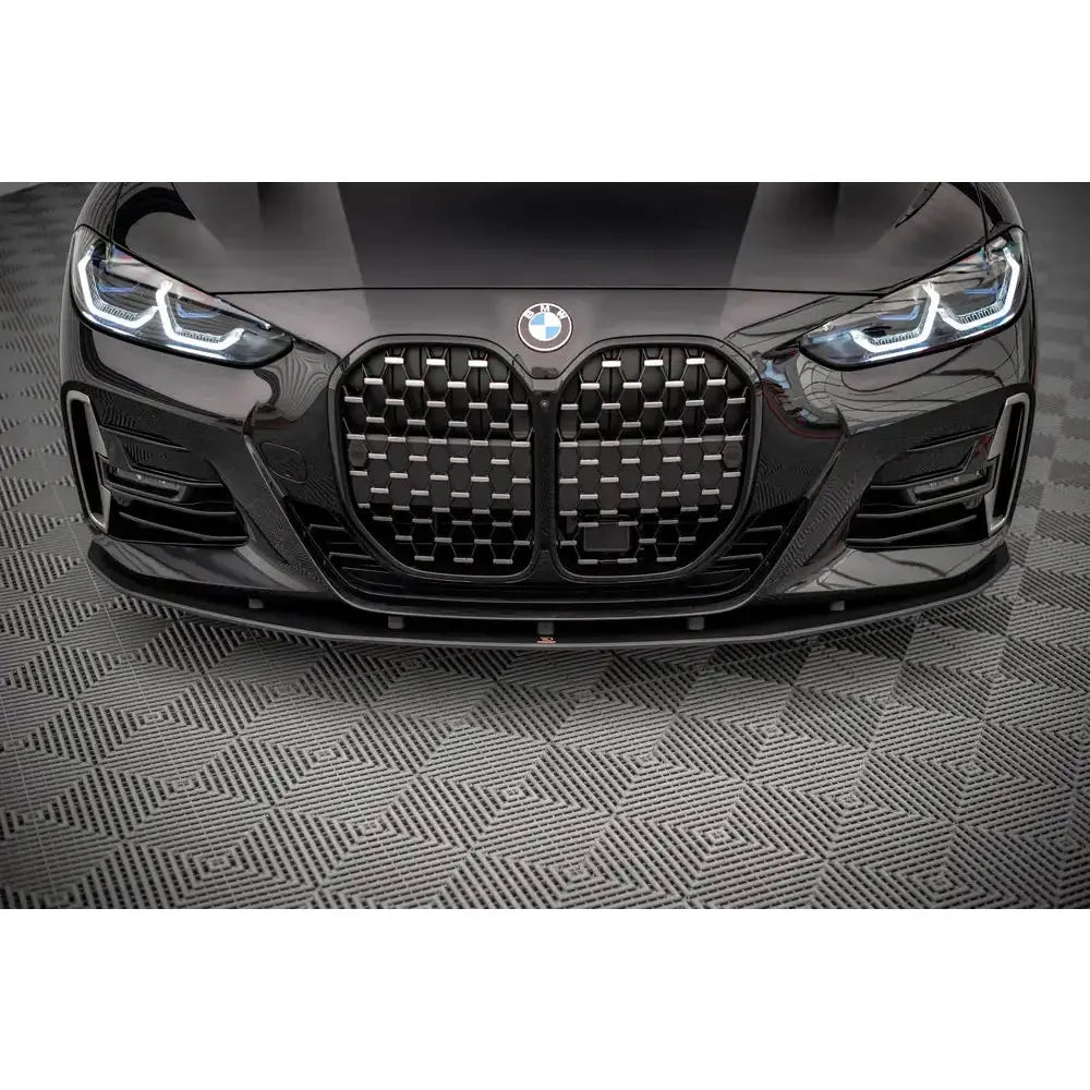 Frontleppe på sort BMW 4 M-Pack G22 med markert grill og skarpe frontlys på grått, mønstret underlag.