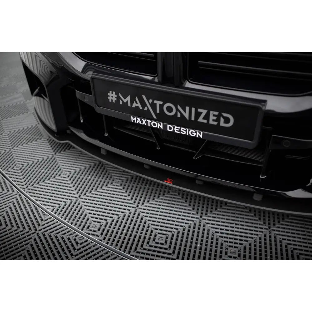 Front splitter BMW M2 G87 Street Pro V1 i blank sort med Maxton Design-logo og rød detalj på grått gulv.