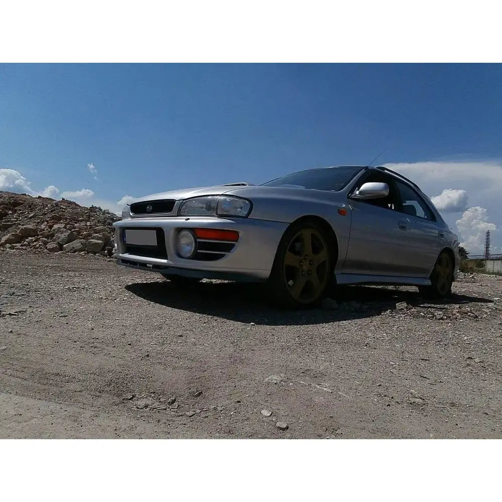 Frontleppe på Subaru Impreza GT med gullfelger og sorte detaljer, fotografert utendørs på grus.