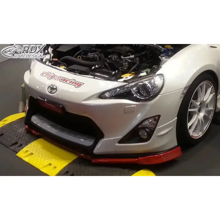 Front splitter på hvit Toyota GT86 Aero med røde detaljer, åpnet panser og synlige hovedlykter.