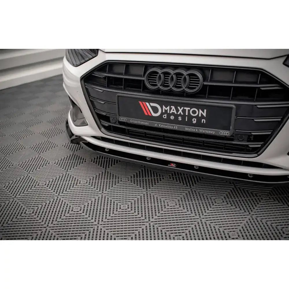 Spoiler Audi A4 B9 Facelift V.1 i sort blank finish montert under frontfanger på hvit bil, lav vinkel.