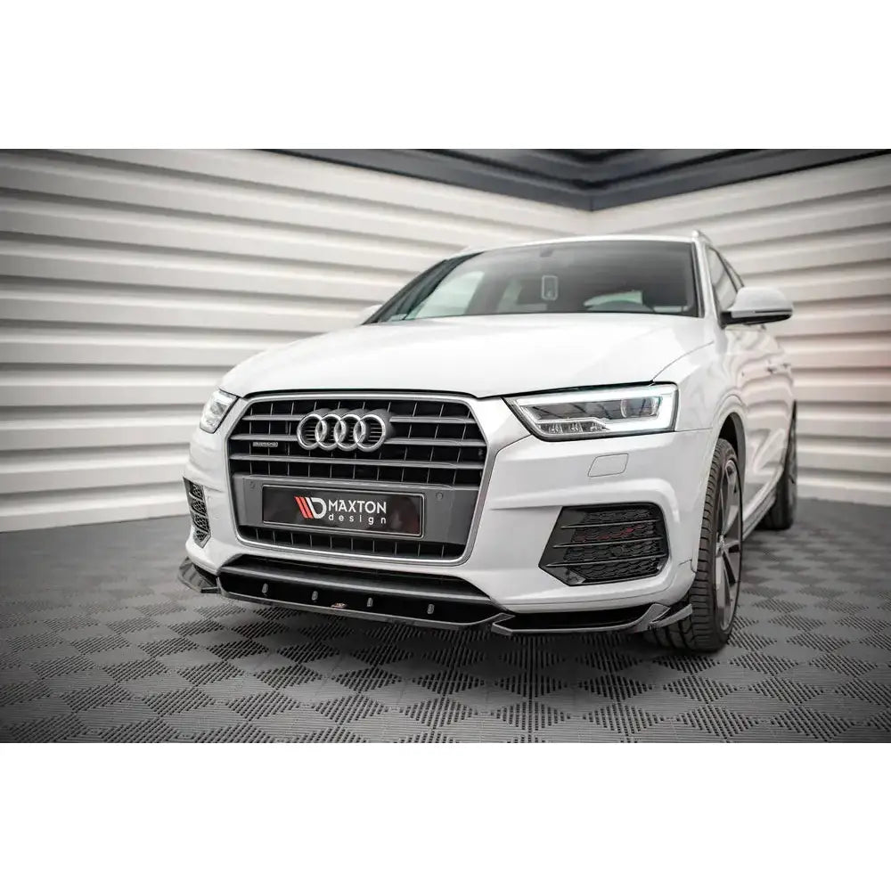 Front splitter på Audi Q3 S-Line 8U Facelift med sort grill og lav spoiler, innendørs mot stripet veggpanel.
