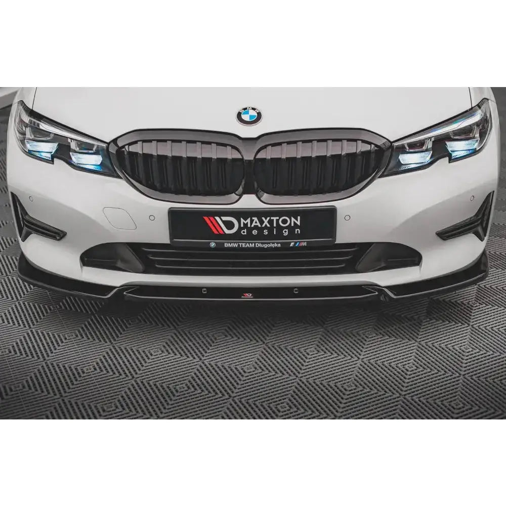 Frontspoiler til BMW 3 G20/G21 V.1 i blank sort, montert på hvit bil, sett rett forfra.