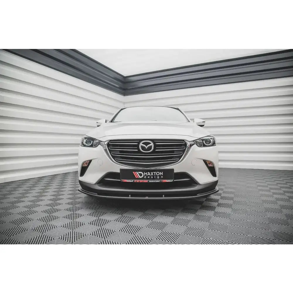 Frontleppe på hvit Mazda CX-3 V.1 15- med kromgrill og sort spoiler, fotografert innendørs.