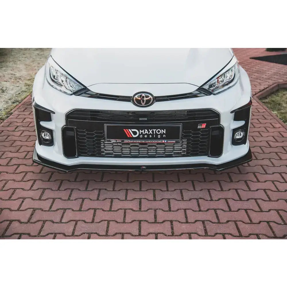 Frontleppe Toyota GR Yaris Mk4 V.1 på hvit bil med svart grill, vist rett forfra mot brosteinsunderlag.