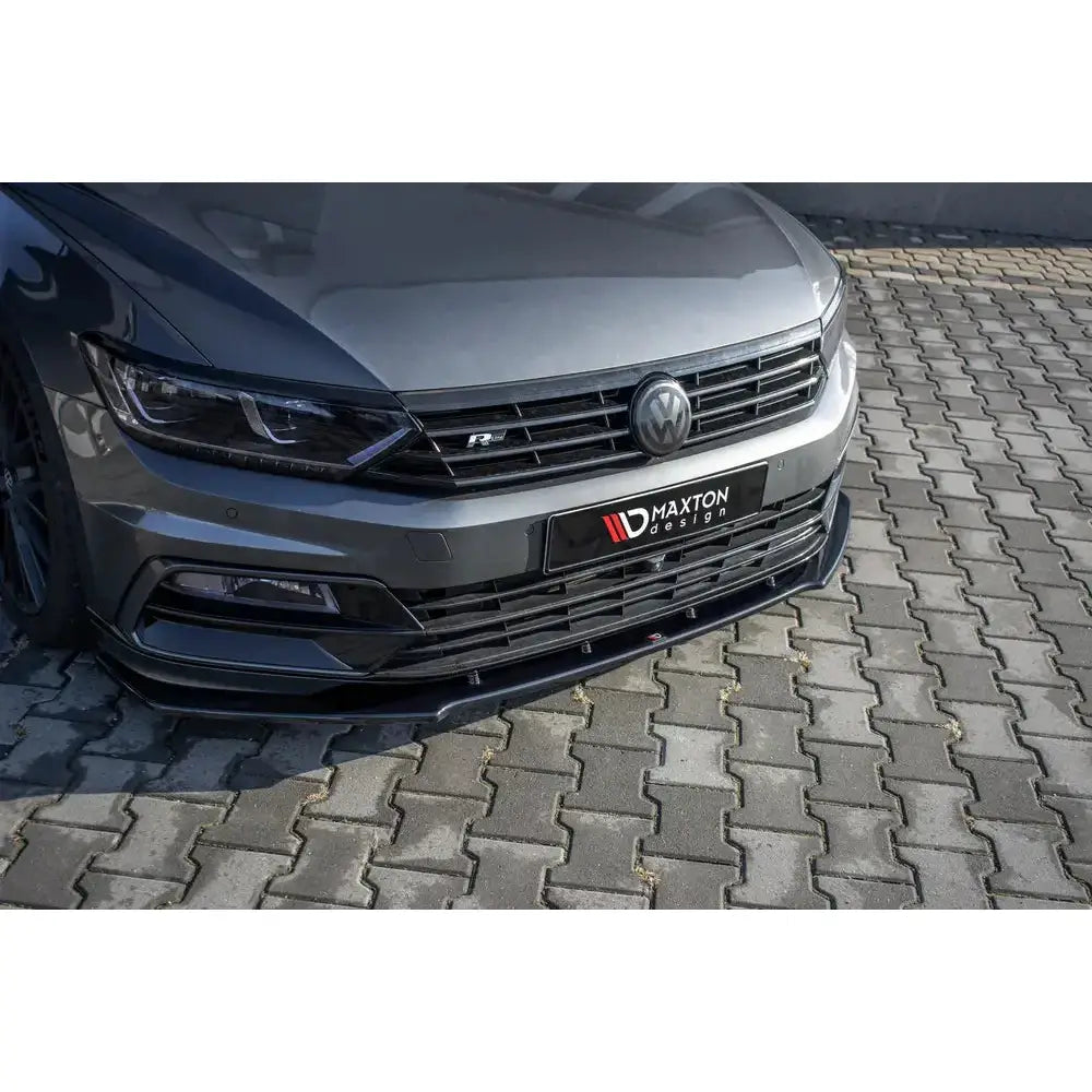 Spoiler til Volkswagen Passat R-Line B8, sort plast, sett forfra på grå bil med synlig logo.