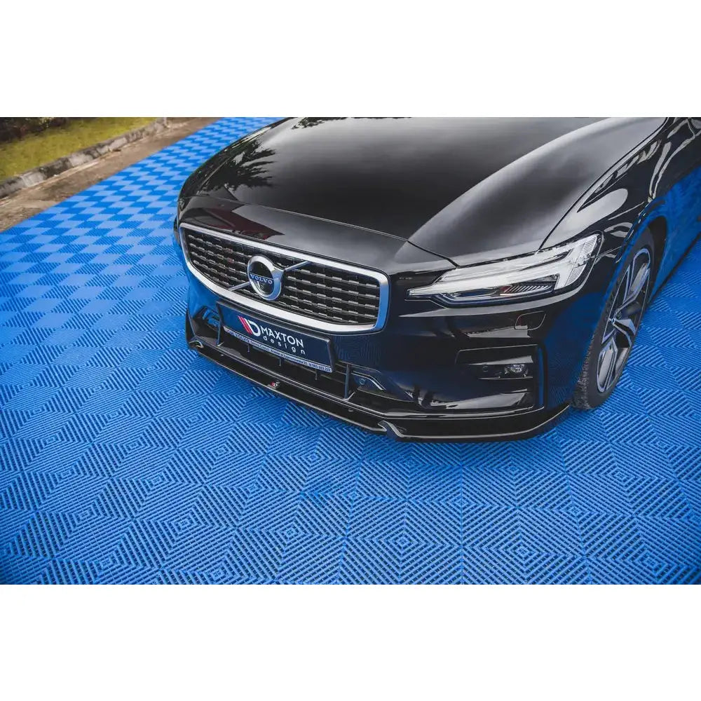 Front splitter på Volvo S60 R-Design Mk3, svart bil parkert på blått gulv med mønster, sett skrått forfra.