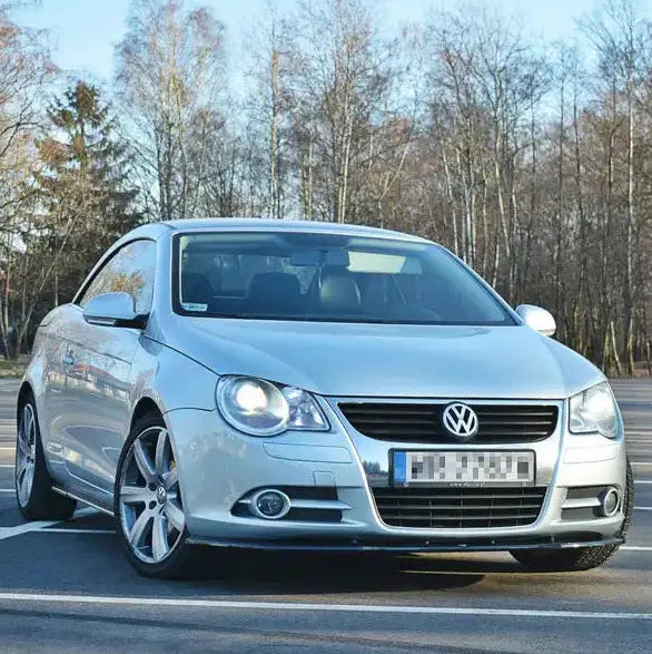 Frontspoiler VW Eos V.1 på sølvfarget bil sett forfra i trekvart vinkel på tom parkeringsplass.
