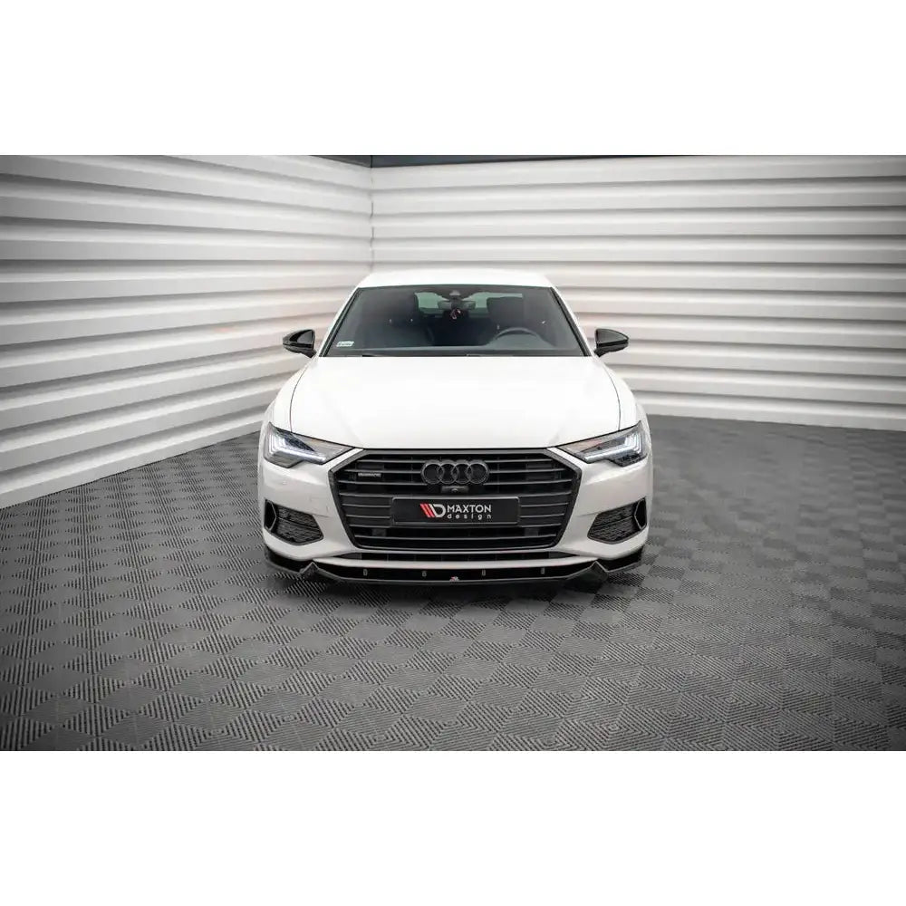 Frontspoiler på hvit Audi A6 C8 sett forfra med mørk grill og LED-frontlykter i lyst rom.