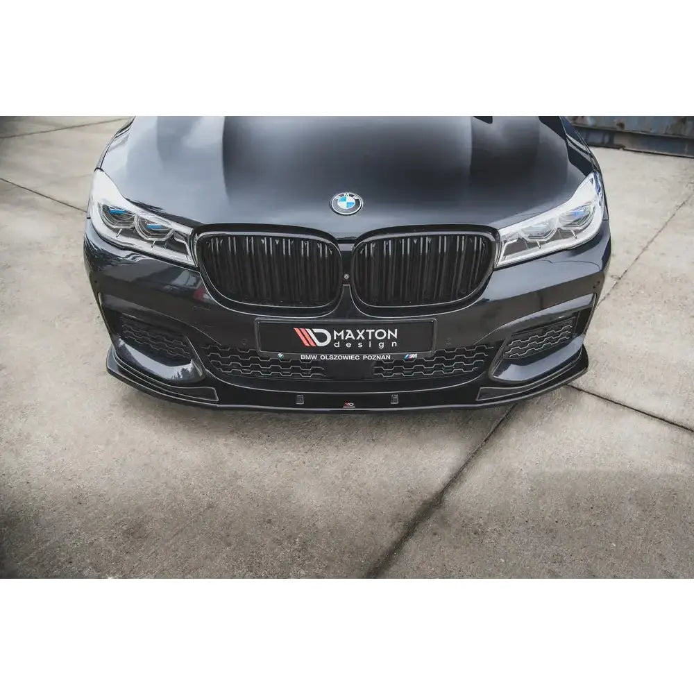 Spoiler på sort BMW 7 G11 M-Pack V.2 med blank svart grill, Maxton Design-logo og betongunderlag.