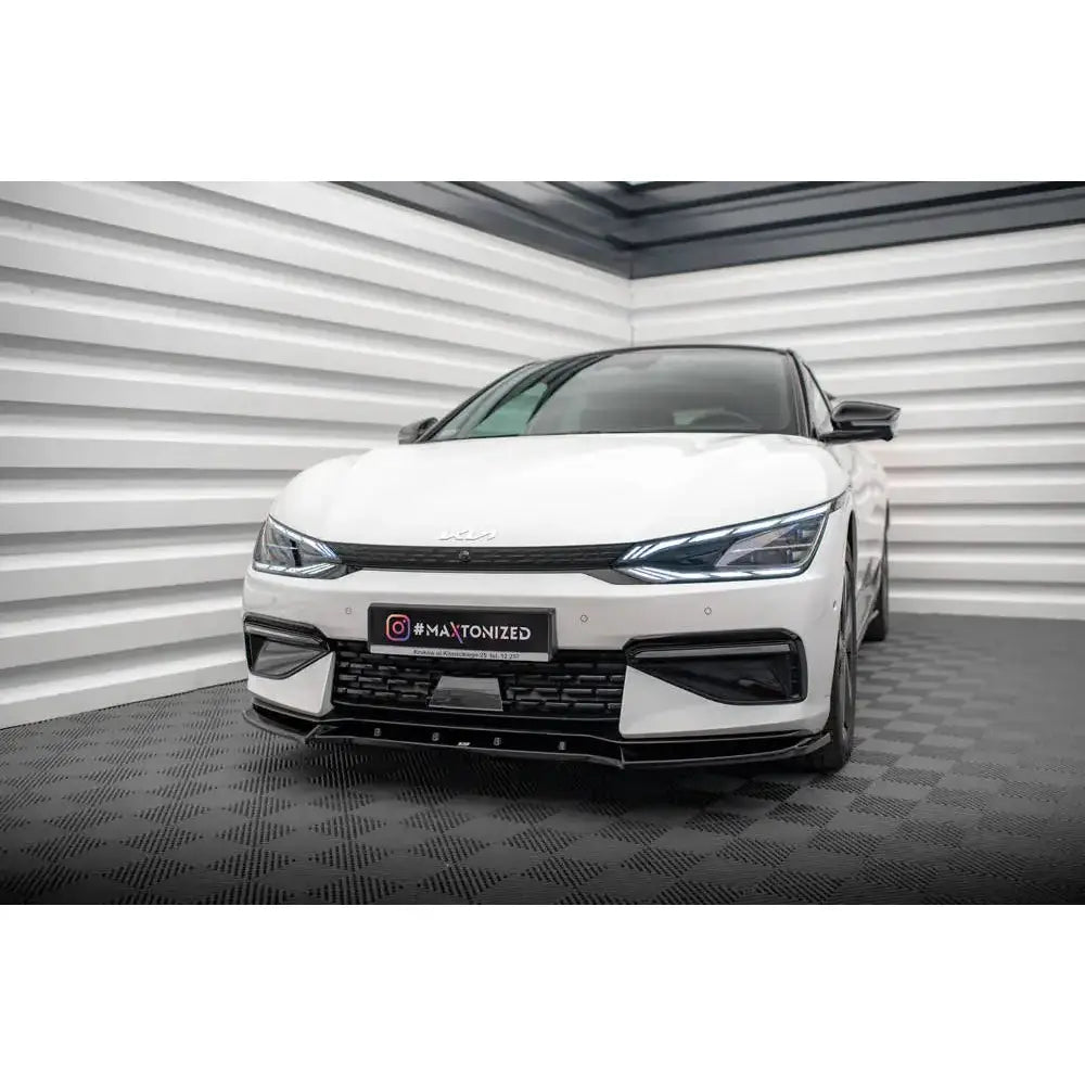 Front splitter på Kia EV6 GT-Line Mk1 V.2 med svarte detaljer og smale LED-lys, sett forfra innendørs.