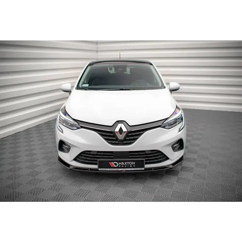 Spoiler til Renault Clio Mk5 V.2 montert foran på hvit bil med tydelig logo, innendørs mot lyse vegger.