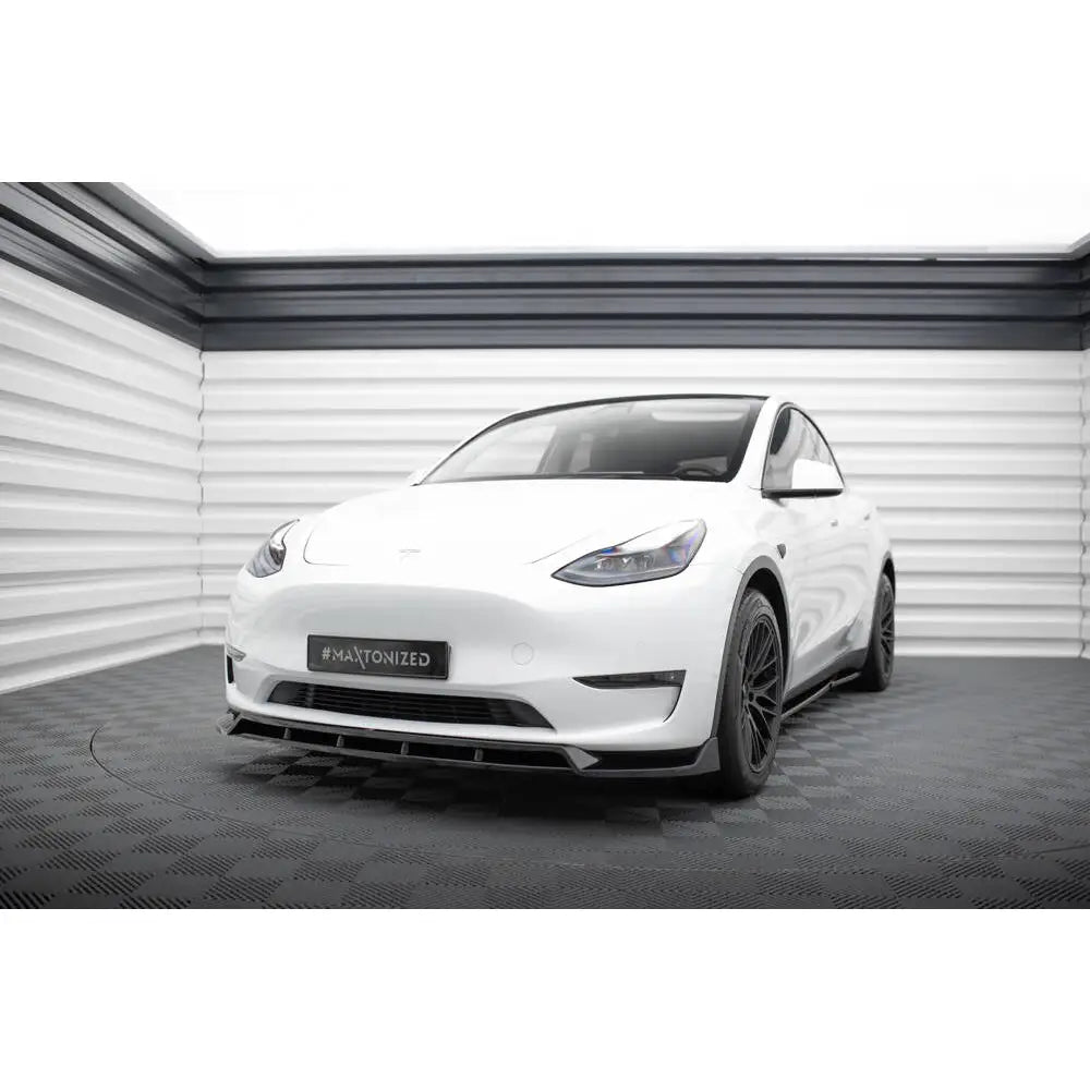Frontleppe på hvit Tesla Model Y V.2 med svarte felger, vist skrått forfra innendørs.
