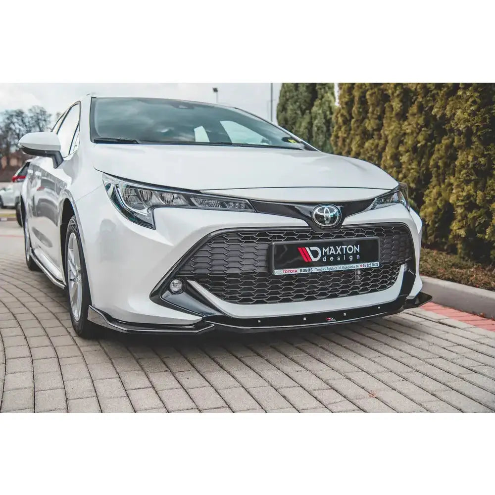 Frontspoiler til Toyota Corolla XII montert på hvit bil med sorte grilldetaljer, utendørs på brostein.