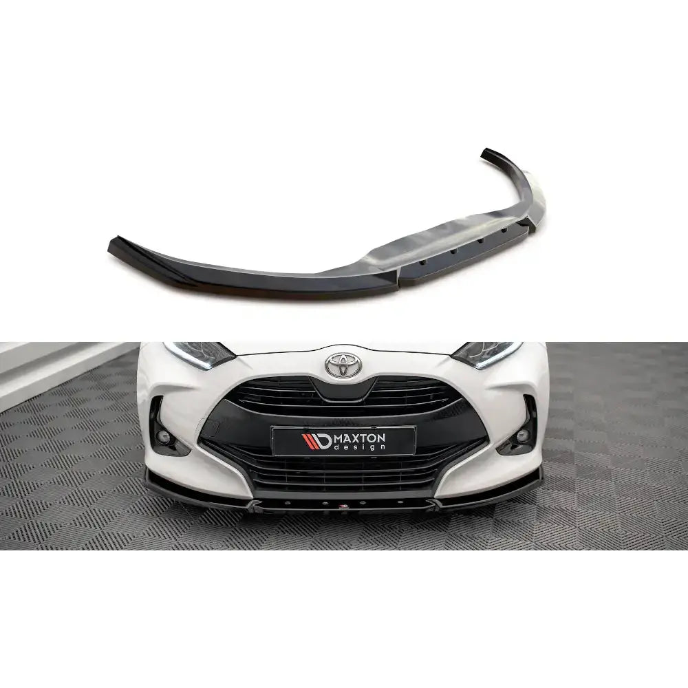 Frontspoiler til Toyota Yaris Mk4 V.2, svart plast, montert på hvit bil med synlige skruedetaljer.