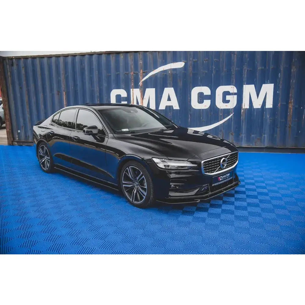 Frontleppe på Volvo S60 R-Design Mk3 V.2 parkert foran blå container på rutemønstret underlag.