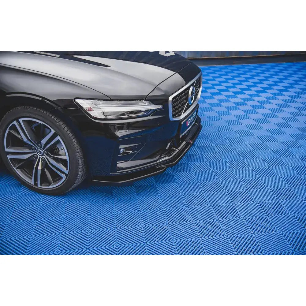 Front splitter for Volvo S60 R-Design Mk3 V.2 på blått diamantmønstret gulv, delvis under svart bil.