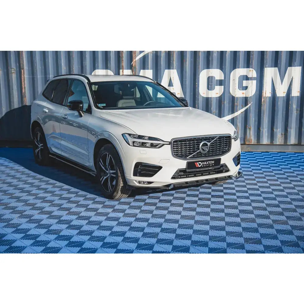 Frontleppe på Volvo XC60 Mk2 V.2 R-Design SUV med svarte detaljer, fotografert foran blå container.
