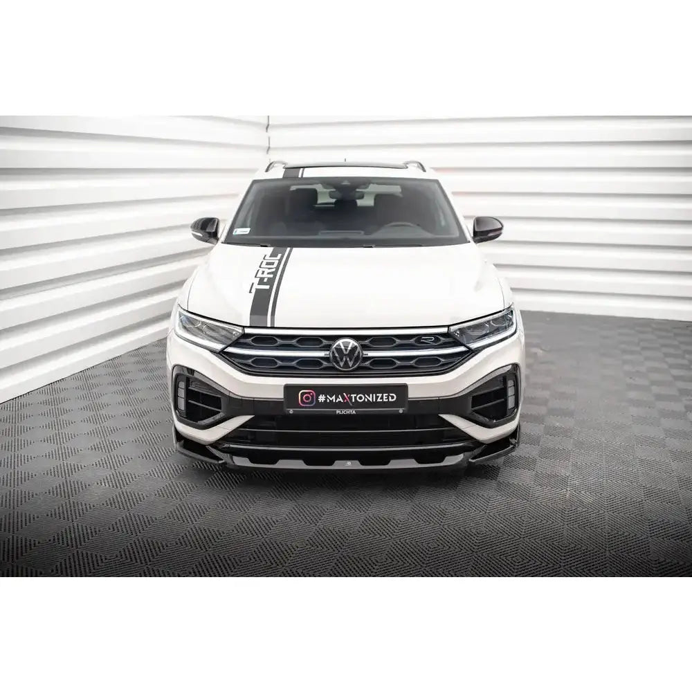 Frontleppe på VW T-Roc R Mk1 Facelift, hvit SUV med svart stripe og detaljer, sett forfra i lyst rom.