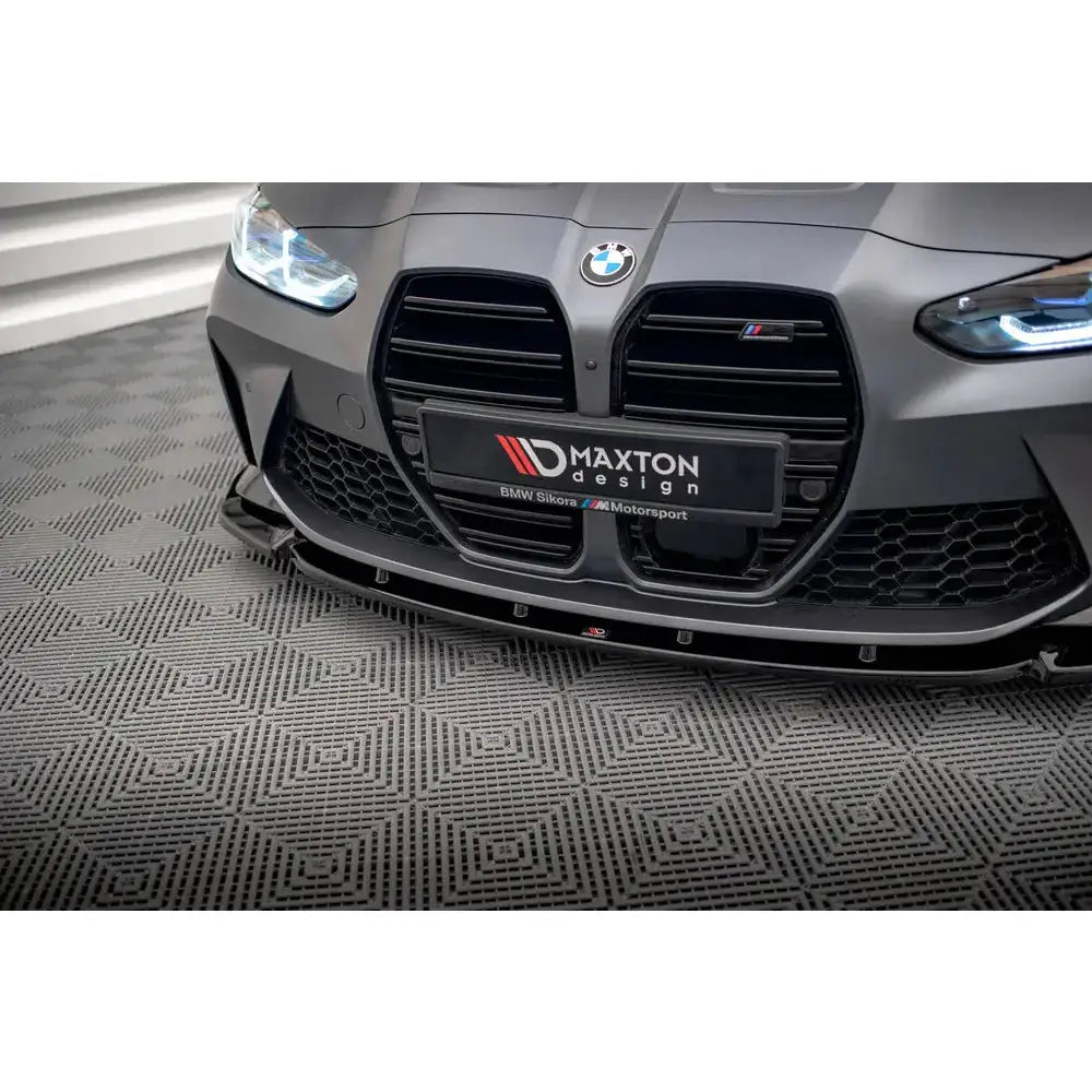 Front splitter til BMW M4 G82 V.3 i sort blank finish montert foran på mattgrå bil mot gulvet.