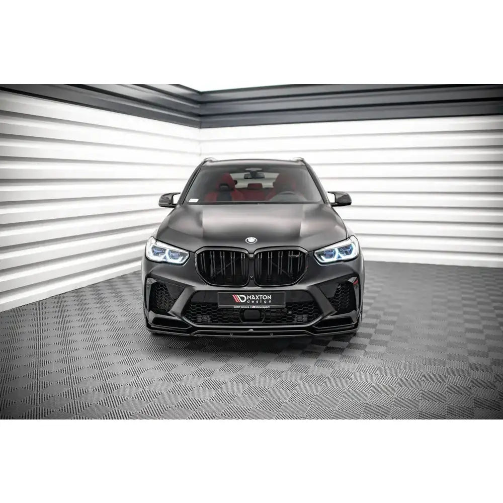 Frontleppe på svart BMW X5M F95 med markante LED-lykter og røde seter, sett forfra i lyst rom.