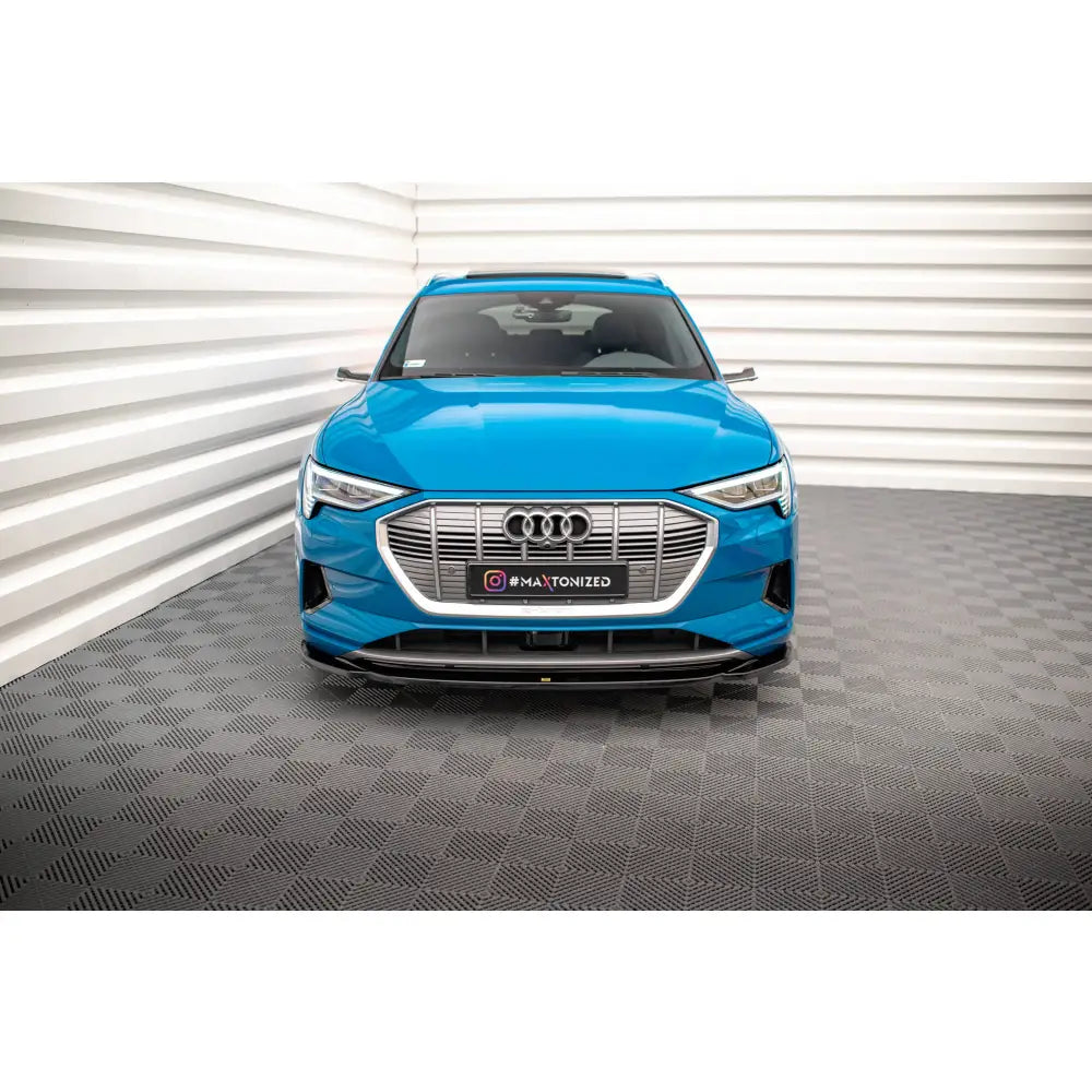 Spoiler på Audi e-tron V1 sett forfra med sølv grill og Audi-logo, innendørs mot hvite vegger.