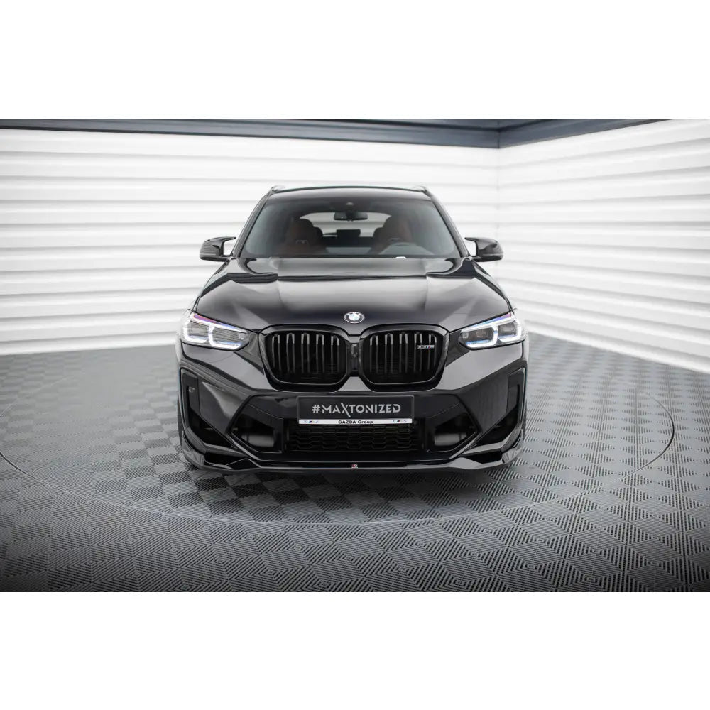 Frontleppe BMW X3 M F97 Facelift V2 sett forfra med sorte detaljer, lys bakgrunn og sjakkmønstret gulv.