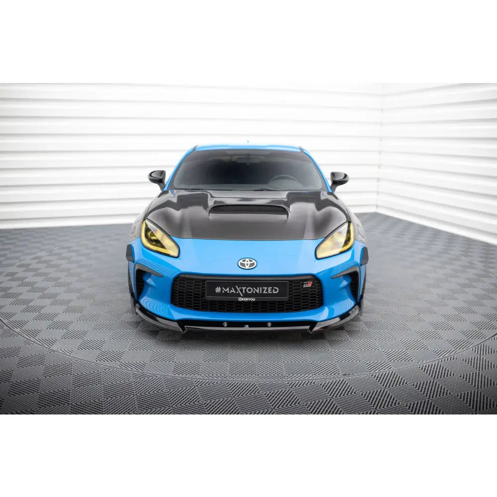 Spoiler på Toyota GR86 Mk1 V3, blå sportsbil med sort panser og gule lykter sett forfra.