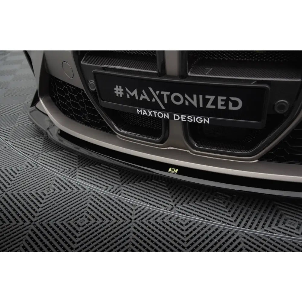 Front lip på BMW M4 G82 V4 CSL Look i glanset sort med #MAXTONIZED-skilt, sett fra skrå vinkel.