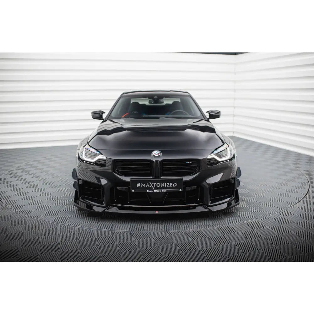 Front splitter BMW M2 G87 V5 montert på svart sportsbil sett rett forfra i lyst rom med mønstret gulv.