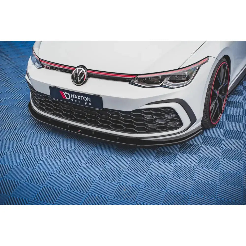 Spoiler til VW Golf 8 GTI, nærbilde av front med sort og rød dekor samt synlig frontsplitter.