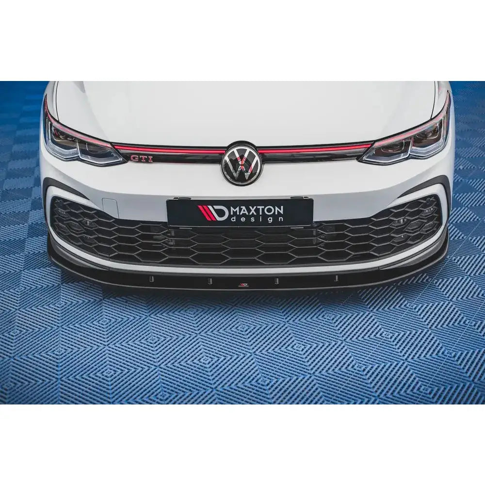 Front lip på VW Golf 8 GTI, sort spoiler med røde detaljer foran hvit bil mot blått gulv.
