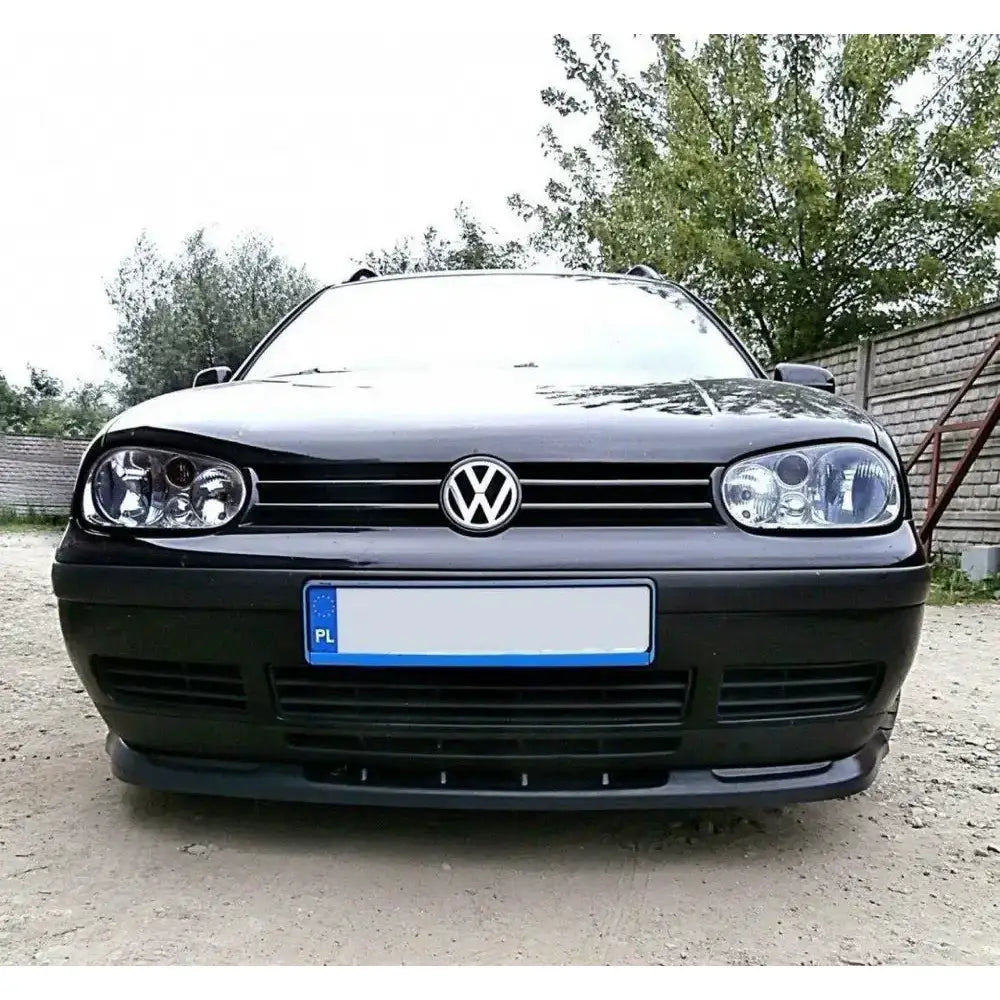 Spoiler på VW Golf IV, sort bil sett forfra med synlig VW-logo, frontlykter og grusunderlag.
